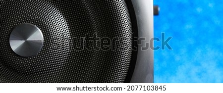 Black hi-end audio speaker with metal grille on a light blue festive background. The concept of music and sound during the party. Macro. Selective focusing. Web banner. Daylight Royalty-Free Stock Photo #2077103845