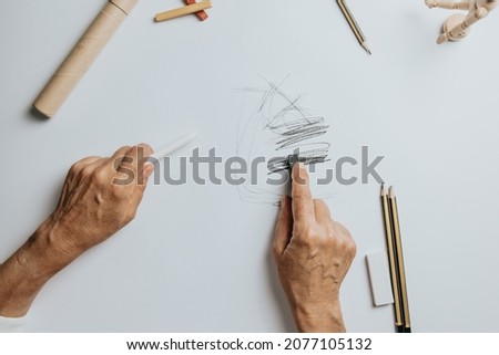 High angle view of a senior Caucasian woman drawing sketches in studio. Creativity, education and people concept,cognitive functions clock drawing self assessment test at home with positive results
