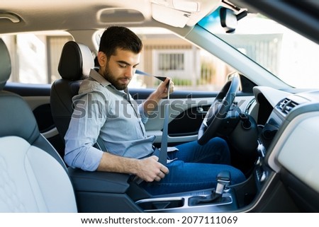 Handsome man putting on the safety seat belt before driving his car to work in the morning Royalty-Free Stock Photo #2077111069