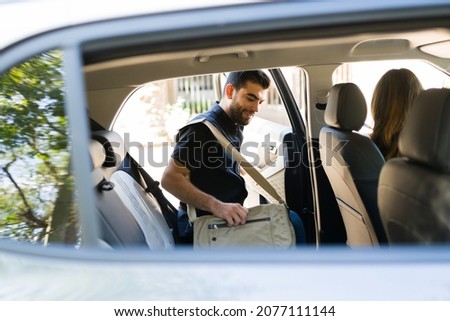Handsome male passenger smiling and getting on a rideshare car while talking to the female driver  Royalty-Free Stock Photo #2077111144