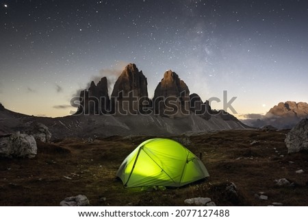 Green tent lighted from the inside against the backdrop of incredible starry sky and Three Peaks of Lavaredo mountains. National Park Tre Cime di Lavaredo, Dolomites, Italy. Landscape photography