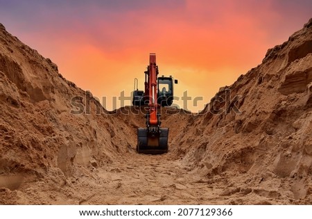 Excavator dig trench on sunset background. Backgoe on earthwork. Construction natural gas pipeline. Construction the sewage and drainage.  Laying sewer pipes at construction site. Open pit mining. Royalty-Free Stock Photo #2077129366