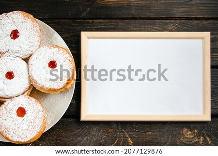Happy Hanukkah. Empty frame for congratulations text and traditional dessert Sufganiyot on dark wooden background. Celebrating Jewish religious holiday.