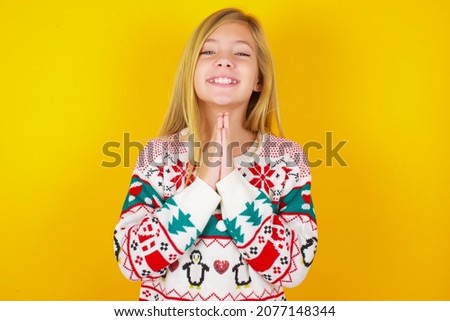 caucasian little kid girl wearing knitted sweater christmas over yellow background praying with hands together asking for forgiveness smiling confident.