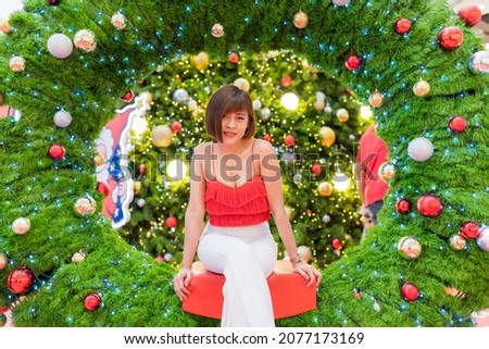 A smart woman model in mini red shirt and white long pants, she acting on lighting for decorate in christmas festival and happy new year on public park, she like and happy on time