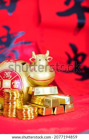 A golden bull piggy bank on a festive red background carrying a pile of gold coins. The Chinese characters in the picture mean "peace and wealth"