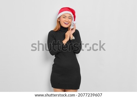 Attractive young Asian woman in Santa Claus hat rubs palms and smile broadly expressed over white background