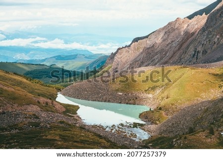 Colorful green landscape with beautiful turquoise mountain lake in sunlight. Impressive scenery with turquoise lake on background of green mountains with forest and low clouds. Scenic mountains view.
