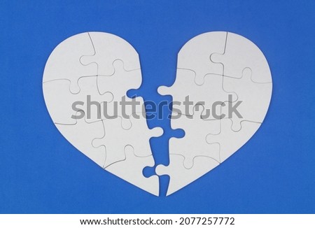 Broken white puzzle heart on blue background. Heart health concept.