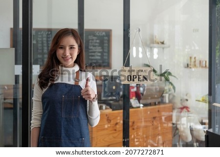 Portrait of a smiling Asian entrepreneur standing behind her cafe counter with open sign board