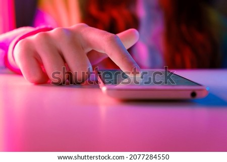 Use of mobile phone in trendy neon lights. Creative vivid color of ultraviolet red and blue. Hands of Teen Girl scrolling up photos Close-up at dark neon room. App for sale in shop. Social media. 4K