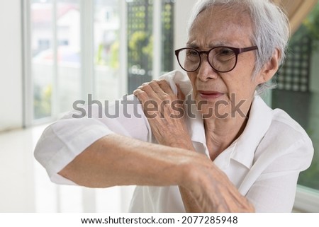 Asian senior woman massage her shoulder bone with hand,aching and tingling,old elderly patient with frozen shoulder,pain and stiffness in the shoulder,degenerative disease,rheumatoid arthritis or gout Royalty-Free Stock Photo #2077285948