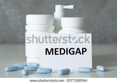 a card with the text MEDIGAP on the table next to white medicine jars and pills in the foreground