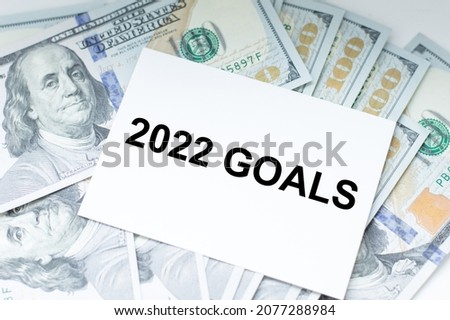 Text 2022 GOALS on the card against the background of dollars on the table. Planning concept.