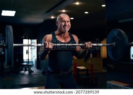  Emotional Bodybuilder older athlete trains in the gym while pumping up biceps muscles. Sporty muscular guy with barbell. Sport and fitness . Individual sports recreation.