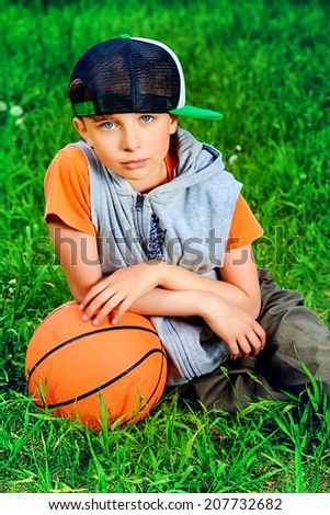 Cool boy lying on a grass with a basketball at a park. Summer day. 