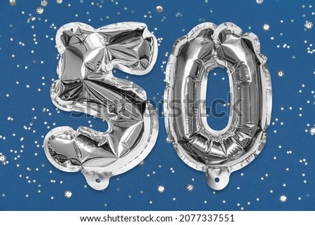 Silver foil balloon number, digit fifty on a blue background with sequins. Birthday greeting card with inscription 50. Anniversary concept. Top view. Numerical digit. Celebration event, template.