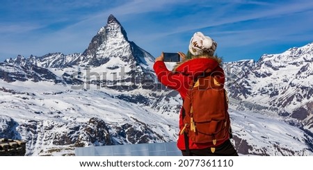 Back view of young woman tourist in red cloth using smartphone taking apicture in Matterhorn mountain ,Swiss apls