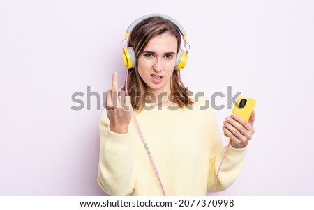 young pretty woman feeling angry, annoyed, rebellious and aggressive. headphones and phone concept