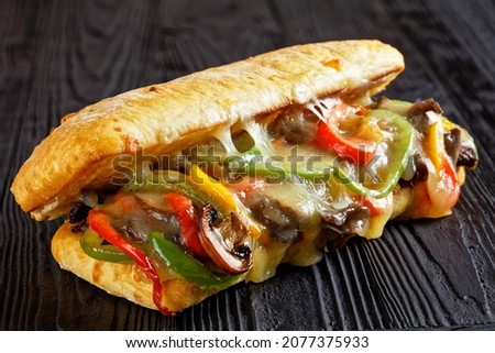 Philly cheese steak sandwich with roasted beef, pepper, caramelized onion, mushrooms and melted cheese on a black wooden table, close-up Royalty-Free Stock Photo #2077375933