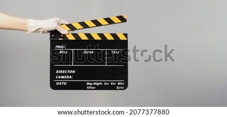 Hand is holding yellow with black clapper board color and wear medical glove.It is used in video production and film industry on grey background.