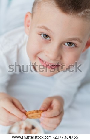 Adorable 6 year old boy in festive pajamas sits by the Christmas tree holding a mug of hot cocoa with marshmallows and lollipop in Christmas decorations. Winter holidays. New Year.