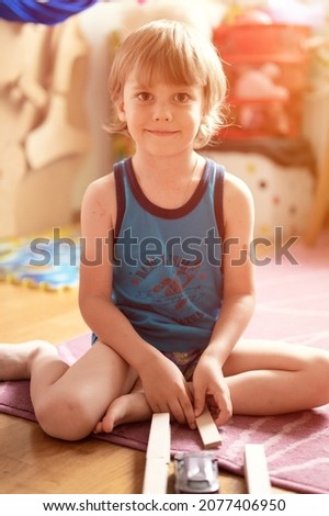 cute little candid five year old kid boy playing at home with children's toys cars and the wooden road on a floor of room in a cozy domestic life. flare
