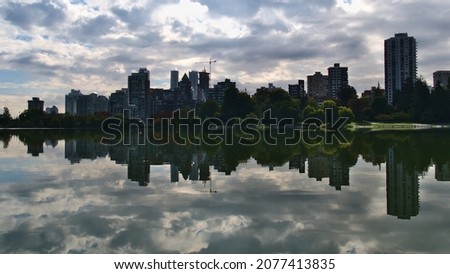 Beautiful view of lake Lost Lagoon in Stanley Park, Vancouver, British Columbia, Canada with the skyline of district Westend reflected in the smooth water on cloudy morning in autumn season.