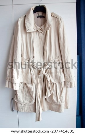 Womens cloak with pockets and a belt hangs on a hanger. Royalty-Free Stock Photo #2077414801