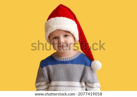 Funny little boy in Santa hat on color background