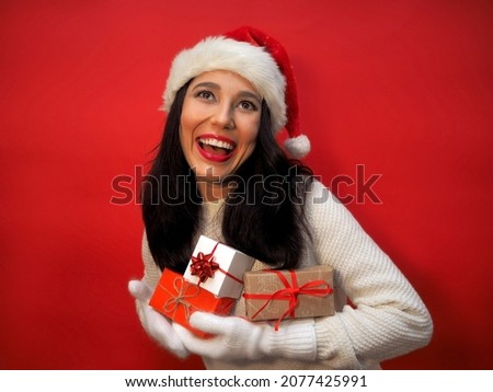 A beautiful girl in a Santa Claus hat rejoices and laughs while holding gifts in her hands. Celebrating New Year and Christmas. The holidays are coming.