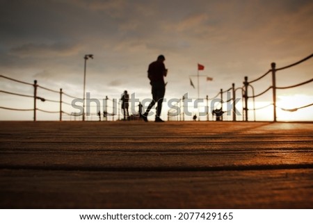 people walk along the pier at sunset
