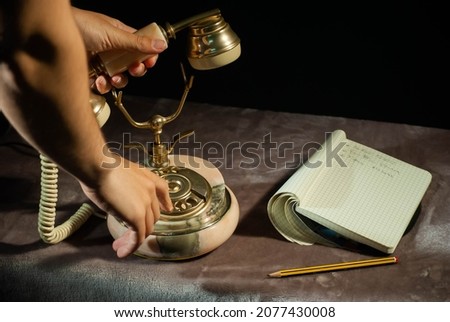 Antique telephone on a table with a small notebook and pencil case. Someone is using the phone