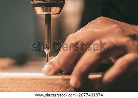 Hand holding a screw while screwing into a wood strip with a drill Royalty-Free Stock Photo #2077431874