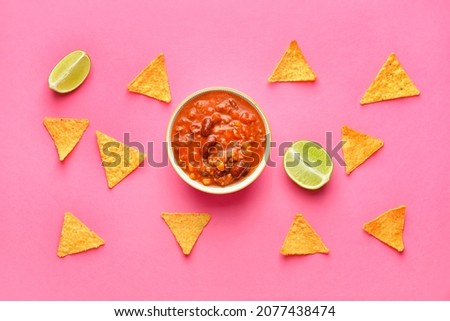 Bowl with tasty chili con carne, lime and nachos on color background