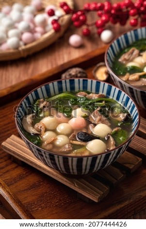 Close up of red and white tangyuan (tang yuan, glutinous rice dumpling balls) with savory soup in a bowl on wooden table background for Winter solstice festival food. Royalty-Free Stock Photo #2077444426