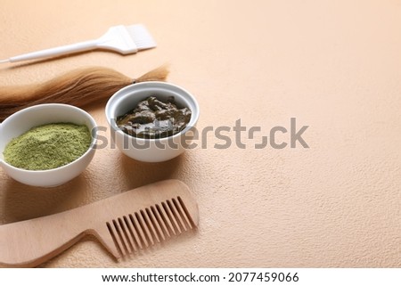 Bowls with henna, hair and comb on color background