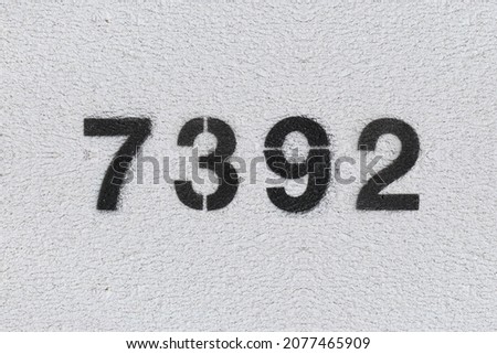 Black Number 7392 on the white wall. Spray paint. Number seven thousand three hundred ninety two.