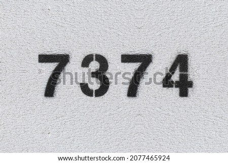 Black Number 7374 on the white wall. Spray paint. Number seven thousand three hundred and seventy four.
