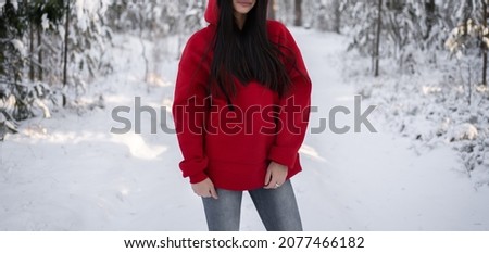 horizontal banner with a model in oversized red hoodie in winter forest.front  view.fashion and wear concept.warm oversize wear at woman.space for text and logo.mock up for print.female standing 