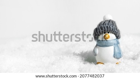 Christmas white snow background, panorama. Happy cute penguin in a winter hat on snowdrifts with hard shadows on the snow. Christmas or New Years concept. Bird penguin in a snowdrift. Banner