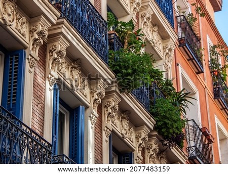 Facade of historical buildings in Madrid, Spain, Europe. Ornaments and balcony with lush green plants. Colorful Mediterranean street scene in Lavapiés, Embajadores neighborhood of the Spanish capital. Royalty-Free Stock Photo #2077483159