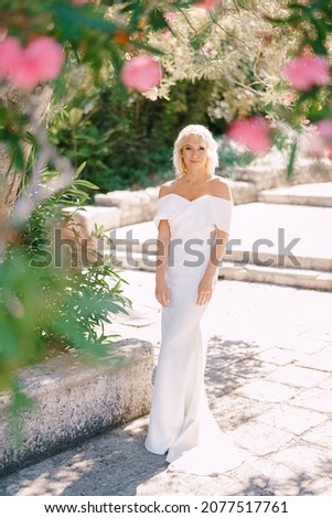 Bride in a white dress stands on a tile in a blooming park