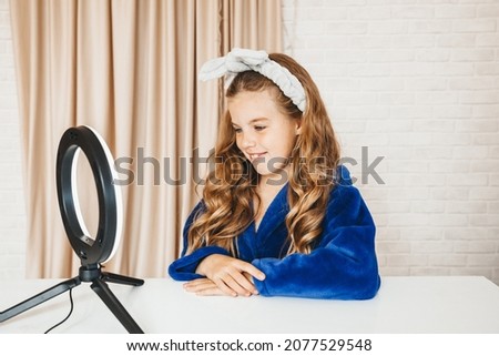 Young happy girl takes pictures of her beauty blog about facial skin care. Child blogger concept. a child stands in front of a light lamp in a bathrobe
