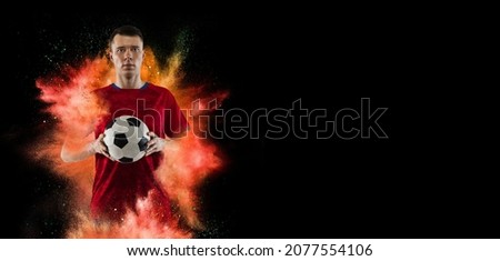 Creative collage of young man, professional football player training isolated over colorful powder explosion on black background. Concept of art, sport, motivation, action. Copy space for ad
