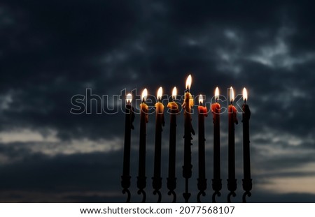 Low key image with burning wax candles as symbol of Hanukkah - Jewish Holiday of Miracle Light. Blurred background of night overcast sky