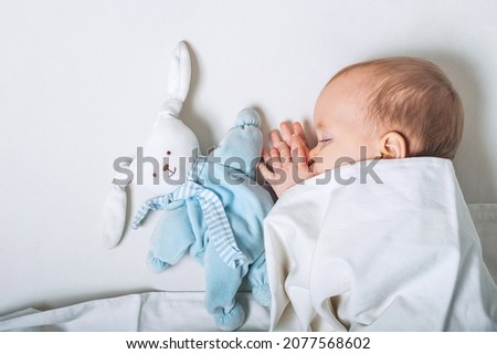 Baby with toy in hands sleeps on bed. Infant development concept, toddler restful sleep, teething, colic.