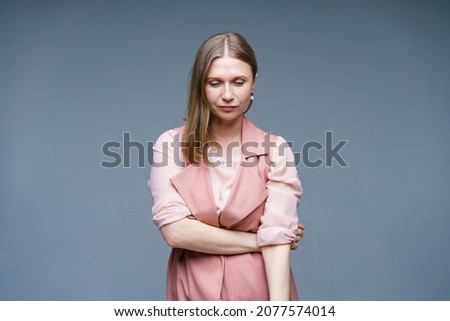 Modest and naive woman with blond hair, stylishly dressed in pink vest and shirt, happy. Studio shot of beautiful pretty woman isolated on studio empty wall background. Royalty-Free Stock Photo #2077574014