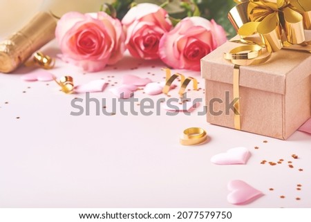 Pink roses flowers, champagne, gift, golden ribbons and confetti red hearts on pink background. Top view flat lay with space for your greetings. Valentines day background and greeting card.