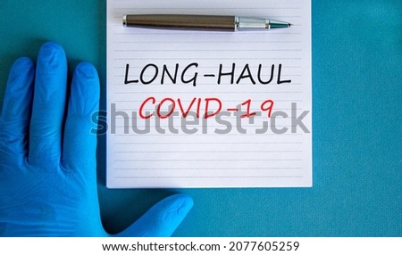 COVID-19 long-haul covid symptoms symbol. White card with words Long-haul covid-19. Doctor hand, pen, blue background, copy space. Medical, COVID-19 long-haul covid-19 symptoms concept.